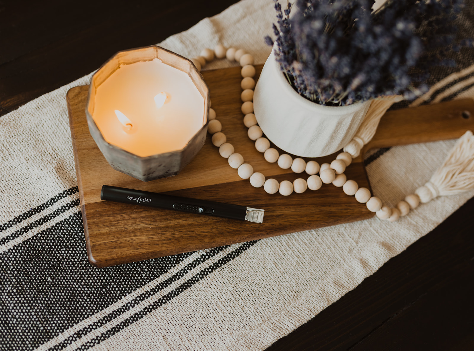 candle, prayer beads and plant pot on wooden board on top of stripe table runner