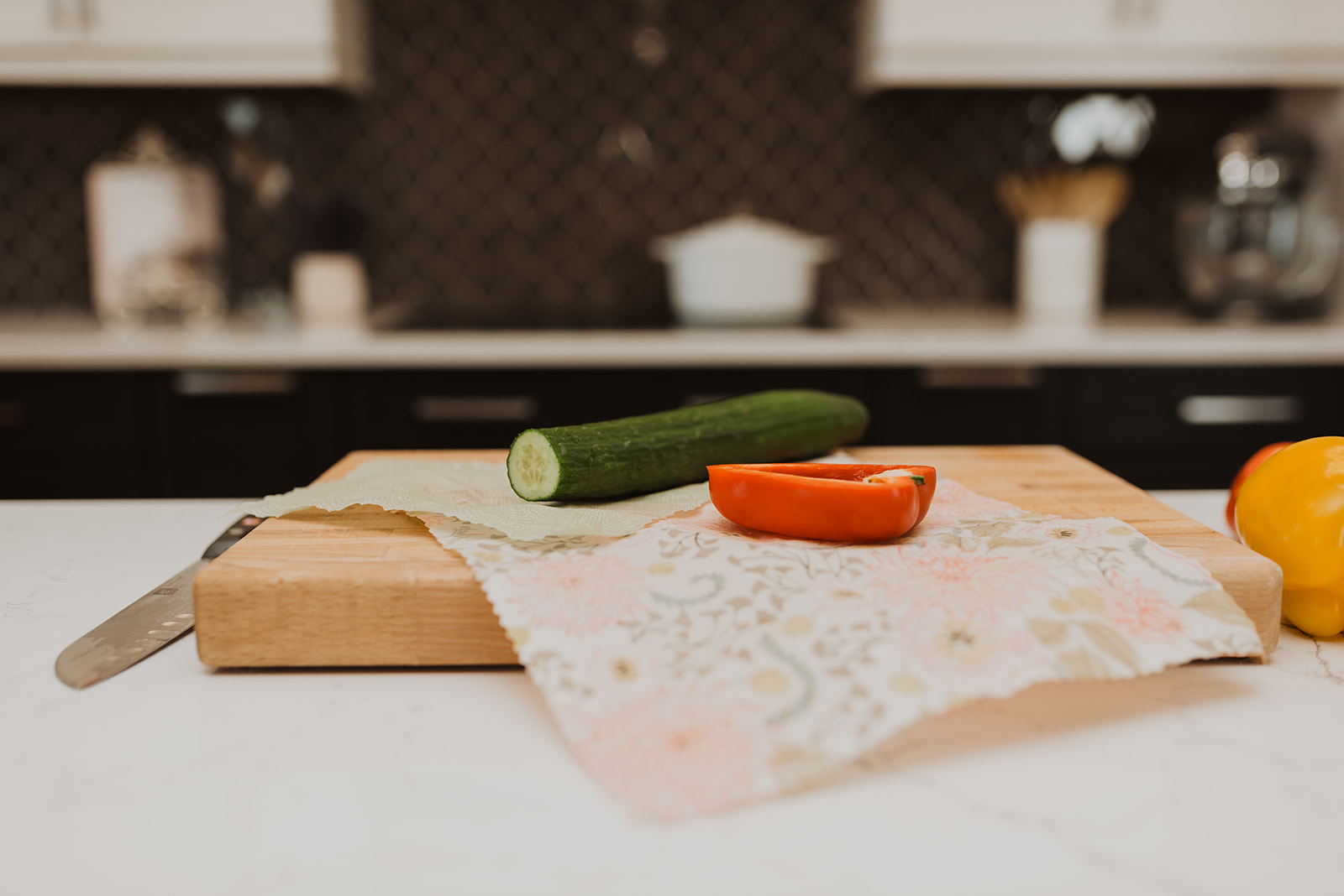 chopping board with cucumber, pepper and floral food wrap in kitchen with black tiles
