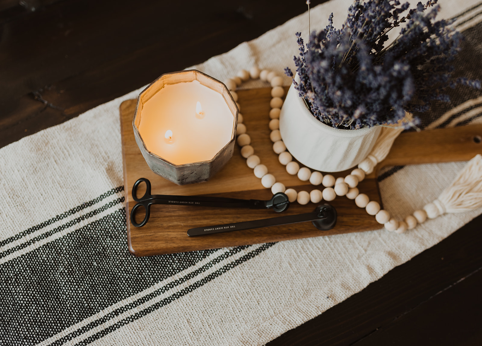 candle, prayer beads and lavender plant on wooden board and stripe table runner